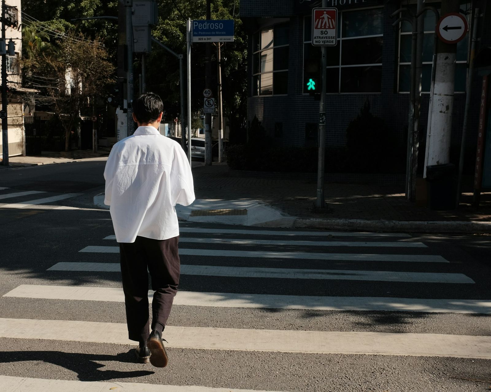A man in a white shirt crossing a city street in morning light